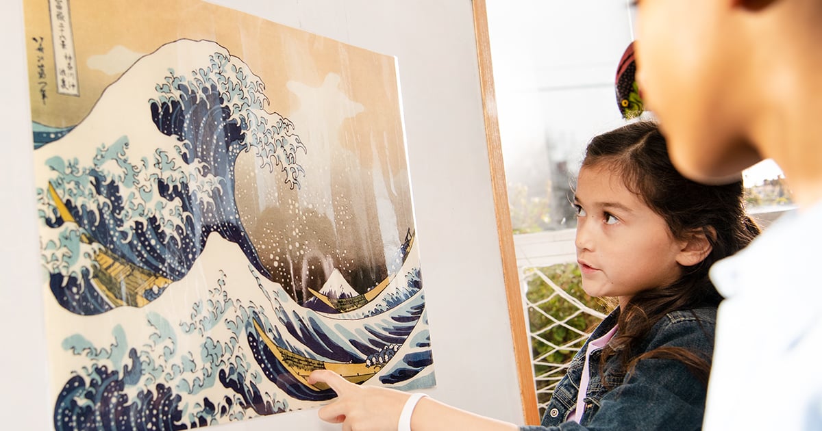 A female student looks at a fine art example from PhD Science as her teacher observes. Fine art pictured is The Wave.