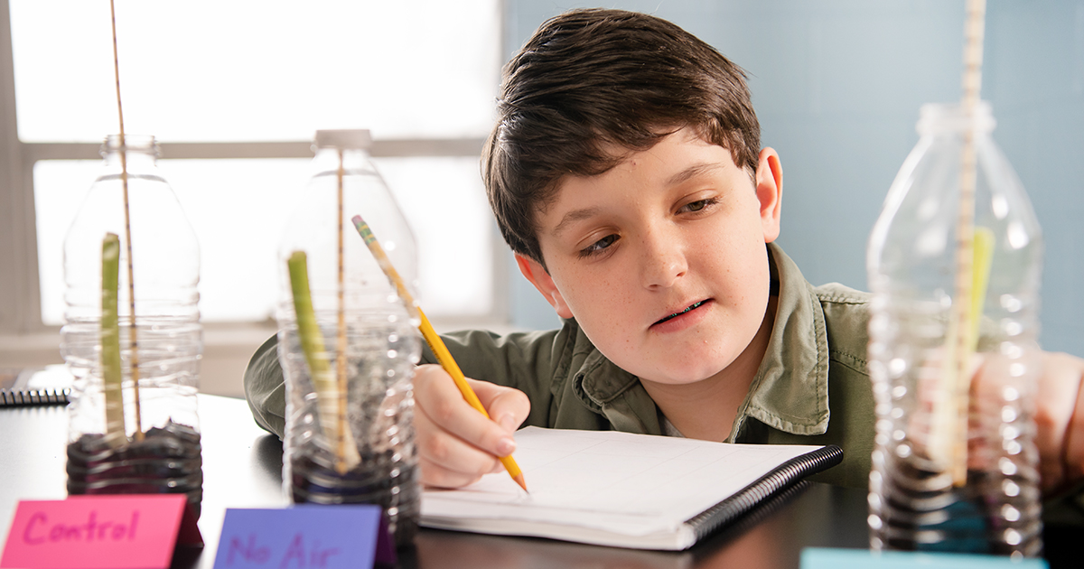 Young student writing in a notebook while doing a science experiment.