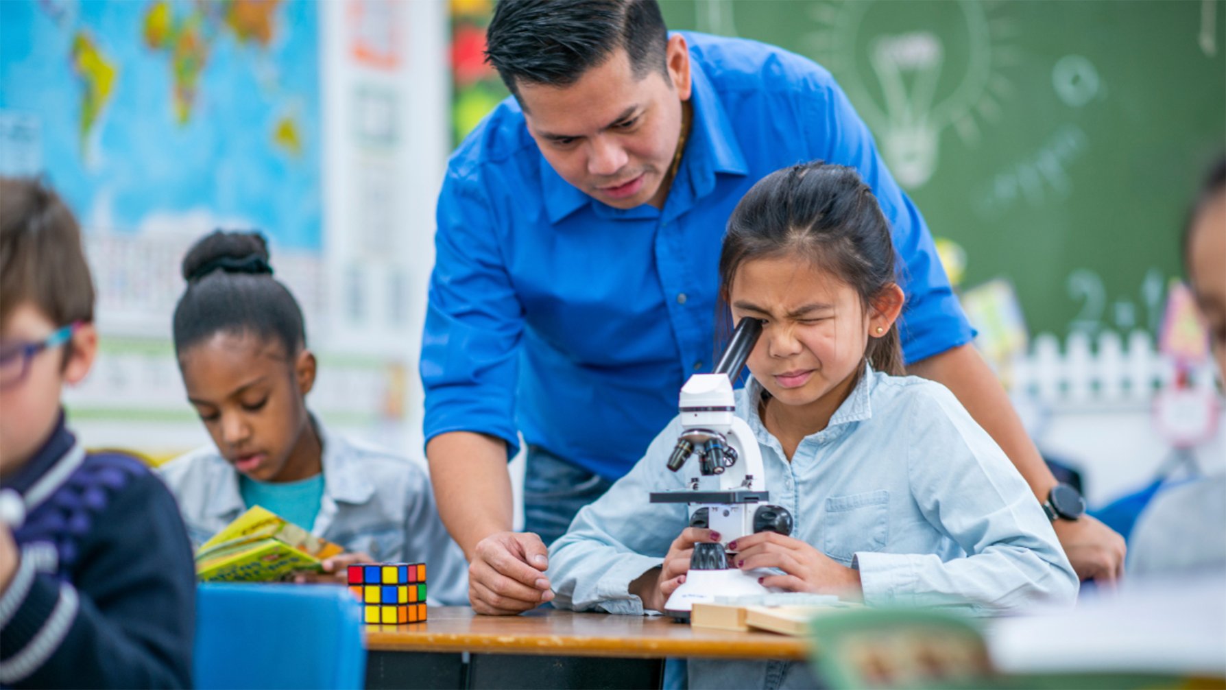 Student looking into a microscope as teacher observes