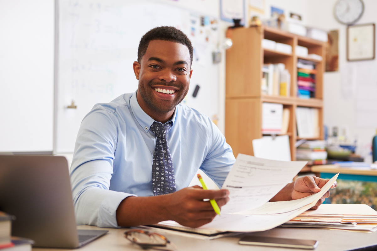 Educator sitting at desk smiling while holding papers in hand