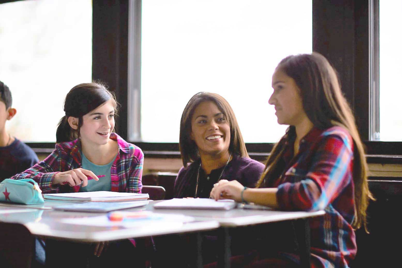 Teacher speaking with students smiling and seated at desk