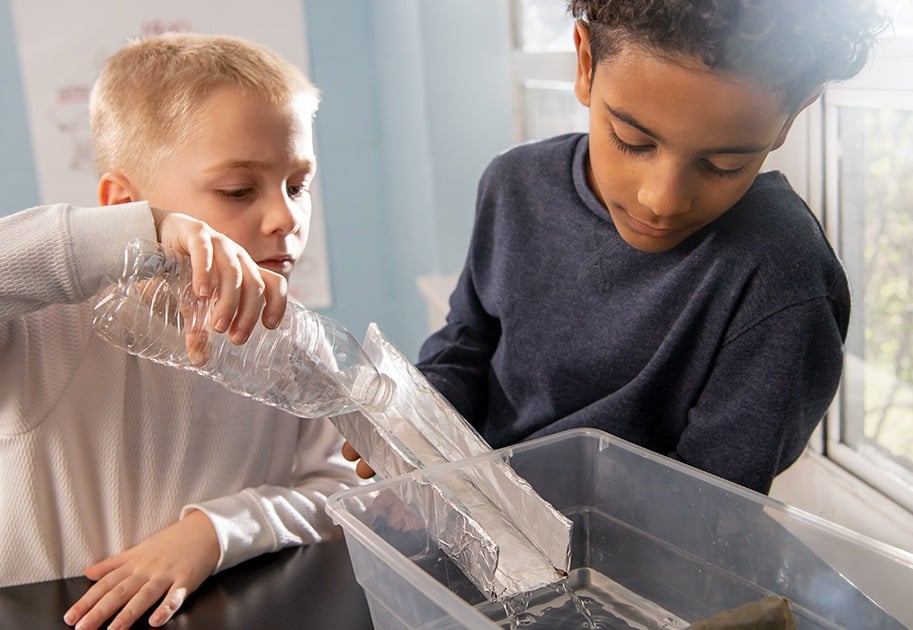 Two male students engaging in a water dam hands-on investigation