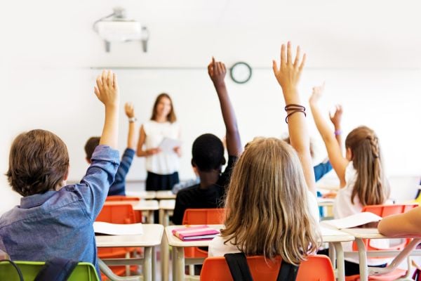 Students raising hands while teacher stands at front of classroom