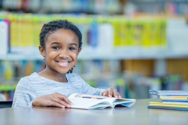 Young student smiling at camera with book open in library